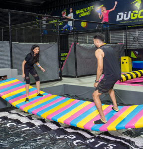 A couple playing on a battle beam at a trampoline park for adults in Chennai.