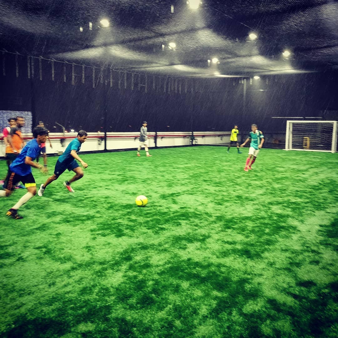 Players chase a football on a rainy day on futsal turf in Chennai.