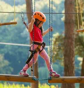 A girl on a rope course with safety guards at an adventure arena Chennai.